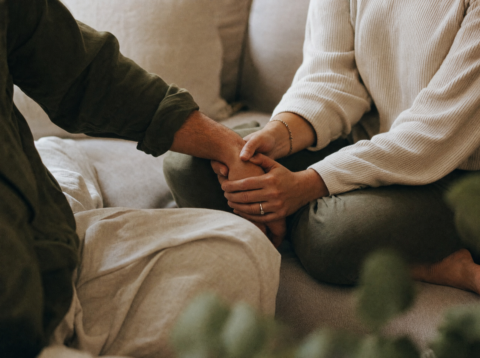 Zwei Menschen halten einander auf dem Sofa die Hände